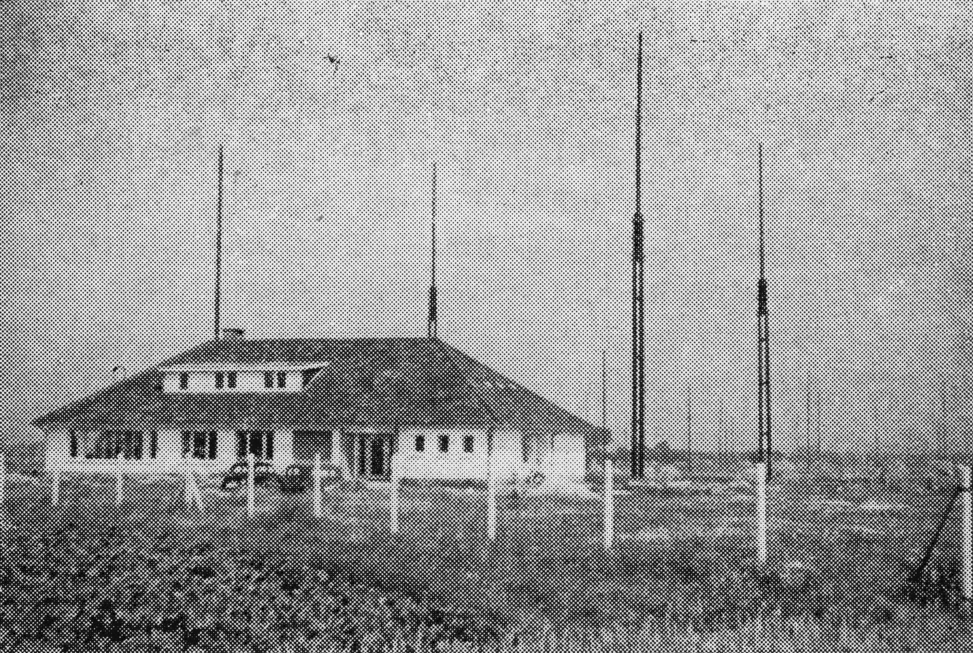 A house-like building in a rural area surrounded by 4 tall masts